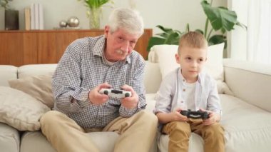 Mutlu bir aile. Yaşlı büyükbaba oğlan torun evde joysticklerle oyun oynuyor. Oyun için oyun bloknotları kullanarak gülümseyen büyükanne ve çocuk. Eski nesil modern teknoloji kullanımı