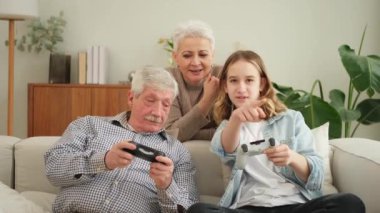 Evde mutlu bir aile. Yaşlı adam büyükbaba kadın büyükanne kız torun evde joysticklerle oyun oynuyor. Oyun için gamepad kullanan iki nesil büyükbaba ve ergen
