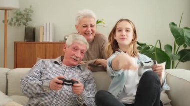 Evde mutlu bir aile. Yaşlı adam büyükbaba kadın büyükanne kız torun evde joysticklerle oyun oynuyor. Oyun için gamepad kullanan iki nesil büyükbaba ve ergen