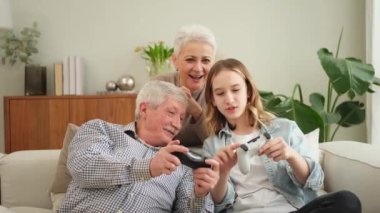 Evde mutlu bir aile. Yaşlı adam büyükbaba kadın büyükanne kız torun evde joysticklerle oyun oynuyor. Oyun için gamepad kullanan iki nesil büyükbaba ve ergen