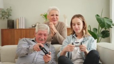 Evde mutlu bir aile. Yaşlı adam büyükbaba kadın büyükanne kız torun evde joysticklerle oyun oynuyor. Oyun için gamepad kullanan iki nesil büyükbaba ve ergen