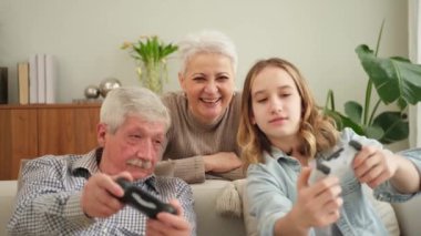 Evde mutlu bir aile. Yaşlı adam büyükbaba kadın büyükanne kız torun evde joysticklerle oyun oynuyor. Oyun için gamepad kullanan iki nesil büyükbaba ve ergen