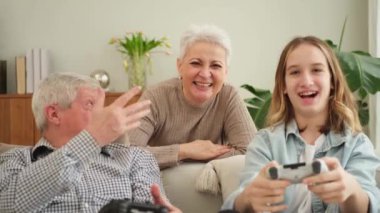 Evde mutlu bir aile. Yaşlı adam büyükbaba kadın büyükanne kız torun evde joysticklerle oyun oynuyor. Oyun için gamepad kullanan iki nesil büyükbaba ve ergen