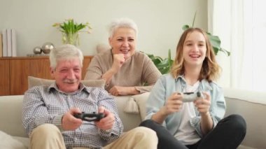 Evde mutlu bir aile. Yaşlı adam büyükbaba kadın büyükanne kız torun evde joysticklerle oyun oynuyor. Oyun için gamepad kullanan iki nesil büyükbaba ve ergen