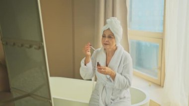 Cilde doğal damla kozmetik yağı süren bir kadın. Yetişkin yaşlı bir kadın günlük güzellik rutini yapan pipetli anti-yaş serumu uyguluyor. Yaşlı kadın yüz bakımı yaptırıyor.