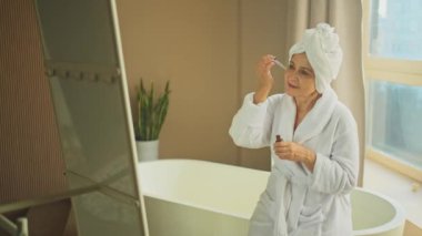 Cilde doğal damla kozmetik yağı süren bir kadın. Yetişkin yaşlı bir kadın günlük güzellik rutini yapan pipetli anti-yaş serumu uyguluyor. Yaşlı kadın yüz bakımı yaptırıyor.