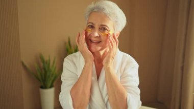 Göz bandı güzellik tedavisi. Kolajen pedleri altında yetişkin bir kadın. Göz altı yamalı yaşlı kadın yüz bakımı yaptırıyor. Son sınıftaki bayan banyoda dinleniyor.