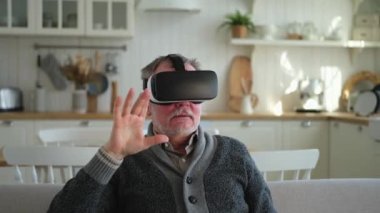 Evde sanal gerçeklik metavers VR gözlük takan heyecanlı olgun bir adam. Dedem sanal gerçeklik miğferinde sanal gerçeklik deneyimi sırasında havaya dokunuyor. Benzetim yüksek teknolojili video oyunu
