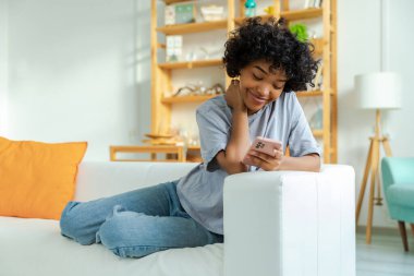 African girl holding smartphone touch screen typing scroll page at home. Woman with cell phone surfing internet using social media apps playing game. Shopping online Internet news cellphone addiction