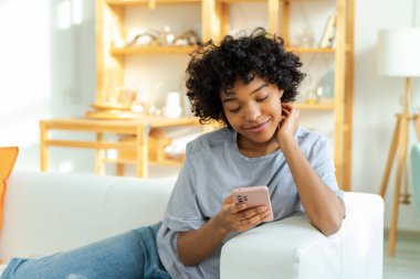 African girl holding smartphone touch screen typing scroll page at home. Woman with cell phone surfing internet using social media apps playing game. Shopping online Internet news cellphone addiction