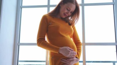 Hamilelik anneliği insanların gelecek beklentisi. Evinin penceresinin yanında koca göbekli hamile bir kadın var. Karnına sarılan ve hamileliğin tadını çıkaran bir kız. Annelik şefkati ebeveynlik yeni yaşam konsepti