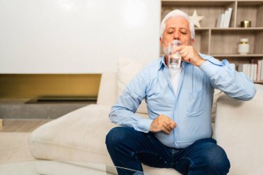 Evde bardak tutan kıdemli adam tatlı su içiyor. Olgun, yaşlı, yaşlı, susamış büyükbaba sağlığıyla ilgilenir. Sağlık hizmeti su dengesi. Yaşlı sağlıklı yaşam tarzı