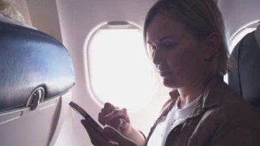 Yolcu kadın uçakla geliyor. Uçak penceresinin yanında oturan telefonu kullanan bir kız. Uçuşun tadını çıkaran akıllı telefonlu gezgin bir kadın. Gemide kablosuz bağlantı kullanan bir kadın var. Gezgin kız.