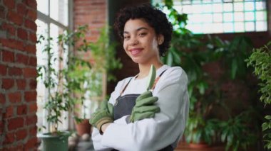 Kendi işimi yürütüyorum. Botanik mağazasında yeşil bitkilerle önlük giyen Afrikalı bir çiçekçi kadın. Çiçekçide çalışan mutlu küçük işletme sahibi etrafı bitkilerle çevrili gülümsüyor.