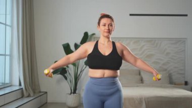 Fitness antrenmanı. Dambılları kaldıran kadın. Artı ev içinde spor egzersizi yapan beden bir kadın. Spor giyimli kız kilo vermek için ağırlık çalışması yapıyor. Spor ve zindelik