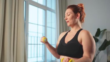 Fitness antrenmanı. Dambılları kaldıran kadın. Artı ev içinde spor egzersizi yapan beden bir kadın. Spor giyimli kız kilo vermek için ağırlık çalışması yapıyor. Spor ve zindelik