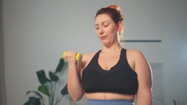 Fitness antrenmanı. Dambılları kaldıran kadın. Artı ev içinde spor egzersizi yapan beden bir kadın. Spor giyimli kız kilo vermek için ağırlık çalışması yapıyor. Spor ve zindelik