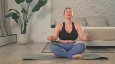 Yoga farkındalığı meditasyonu. Evde yoga yapan bir kadın. Artı nilüfer çiçeğinin üzerinde oturan kadın meditasyon yapıyor içeride rahatlarken gülümsüyor. Nefes egzersizi yapan bir kız. Evde yoga.