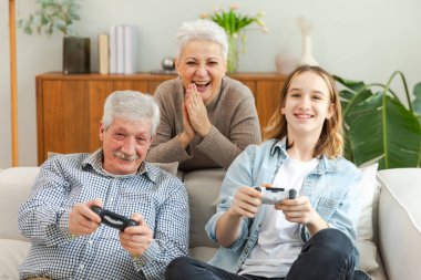 Evde mutlu bir aile. Yaşlı adam büyükbaba kadın büyükanne kız torun evde joysticklerle oyun oynuyor. Oyun için gamepad kullanan iki nesil büyükbaba ve ergen