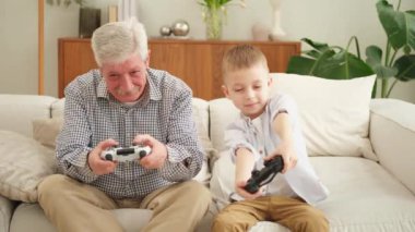 Mutlu bir aile. Yaşlı büyükbaba oğlan torun evde joysticklerle oyun oynuyor. Oyun için oyun bloknotları kullanarak gülümseyen büyükanne ve çocuk. Eski nesil modern teknoloji kullanımı