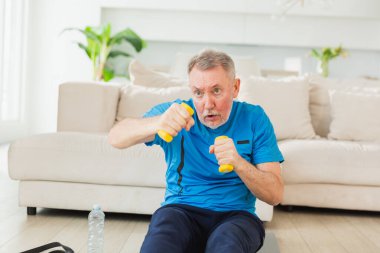 Fitness antrenmanı. Üst düzey boksör dambılları kaldırıyor. Yetişkin, sağlıklı bir adam evde spor yapıyor. Büyükbabanın rehabilitasyonu var. Sağlık hizmetleri