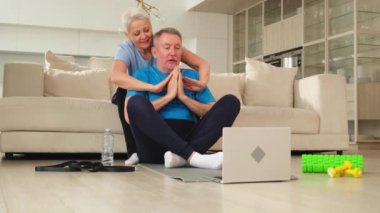 Yoga farkındalığı meditasyonu. Yetişkin bir çift olarak laptopta yoga yapıyoruz. Yaşlı kadın kocaya meditasyon yapmayı öğretiyor. Aile evde nefes egzersizi yapıyor.