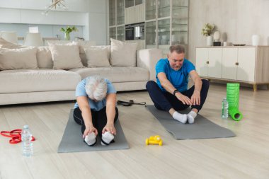 Fitness antrenmanı. Yetişkin, sağlıklı, yaşlı bir çift evde yoga minderinde spor yapıyor. Orta yaşlı koca karısı antrenman yapıyor. Sağlık hizmetleri sağlıklı yaşam tarzı