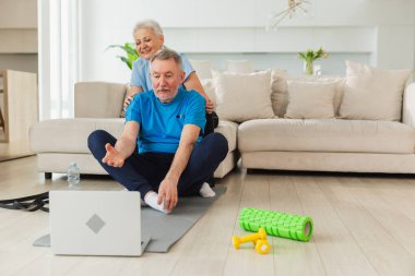 Yoga farkındalığı meditasyonu. Yetişkin bir çift olarak laptopta yoga yapıyoruz. Yaşlı kadın kocaya meditasyon yapmayı öğretiyor. Aile evde nefes egzersizi yapıyor.