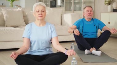 Yoga farkındalığı meditasyonu. Yetişkin bir çift evde yoga yapıyor. Orta yaşlı koca karısı nilüferde oturmuş yoga minderinde meditasyon yaparken poz veriyor. Aile nefes egzersizi yapıyor.