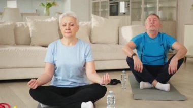 Yoga farkındalığı meditasyonu. Yetişkin bir çift evde yoga yapıyor. Orta yaşlı koca karısı nilüferde oturmuş yoga minderinde meditasyon yaparken poz veriyor. Aile nefes egzersizi yapıyor.