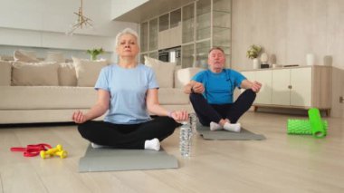 Yoga farkındalığı meditasyonu. Yetişkin bir çift evde yoga yapıyor. Orta yaşlı koca karısı nilüferde oturmuş yoga minderinde meditasyon yaparken poz veriyor. Aile nefes egzersizi yapıyor.