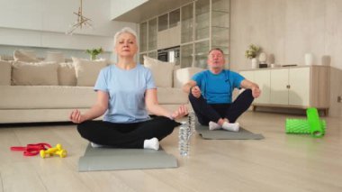 Yoga farkındalığı meditasyonu. Yetişkin bir çift evde yoga yapıyor. Orta yaşlı koca karısı nilüferde oturmuş yoga minderinde meditasyon yaparken poz veriyor. Aile nefes egzersizi yapıyor.