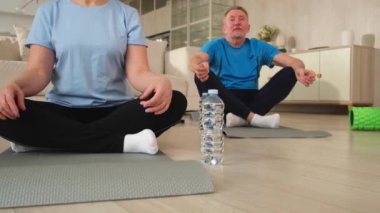 Yoga farkındalığı meditasyonu. Yetişkin bir çift evde yoga yapıyor. Orta yaşlı koca karısı nilüferde oturmuş yoga minderinde meditasyon yaparken poz veriyor. Aile nefes egzersizi yapıyor.