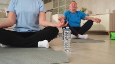 Yoga farkındalığı meditasyonu. Yetişkin bir çift evde yoga yapıyor. Orta yaşlı koca karısı nilüferde oturmuş yoga minderinde meditasyon yaparken poz veriyor. Aile nefes egzersizi yapıyor.