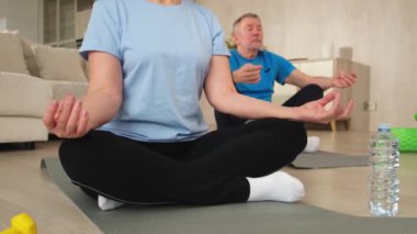 Yoga farkındalığı meditasyonu. Yetişkin bir çift evde yoga yapıyor. Orta yaşlı koca karısı nilüferde oturmuş yoga minderinde meditasyon yaparken poz veriyor. Aile nefes egzersizi yapıyor.