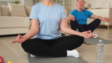Yoga farkındalığı meditasyonu. Yetişkin bir çift evde yoga yapıyor. Orta yaşlı koca karısı nilüferde oturmuş yoga minderinde meditasyon yaparken poz veriyor. Aile nefes egzersizi yapıyor.