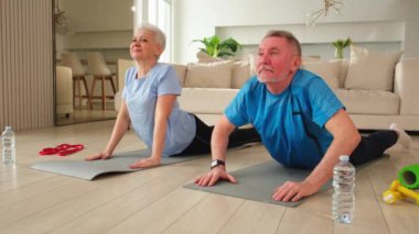Fitness antrenmanı. Yetişkin, sağlıklı, yaşlı bir çift evde yoga minderinde spor yapıyor. Orta yaşlı koca karısı antrenman yapıyor. Sağlık hizmetleri sağlıklı yaşam tarzı