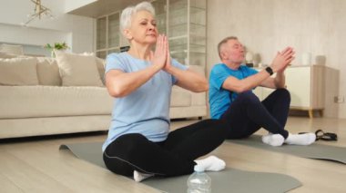 Yoga farkındalığı meditasyonu. Yetişkin bir çift evde yoga yapıyor. Orta yaşlı koca karısı nilüferde oturmuş yoga minderinde meditasyon yaparken poz veriyor. Aile nefes egzersizi yapıyor.