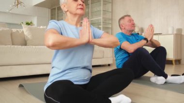 Yoga farkındalığı meditasyonu. Yetişkin bir çift evde yoga yapıyor. Orta yaşlı koca karısı nilüferde oturmuş yoga minderinde meditasyon yaparken poz veriyor. Aile nefes egzersizi yapıyor.