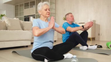 Yoga farkındalığı meditasyonu. Yetişkin bir çift evde yoga yapıyor. Orta yaşlı koca karısı nilüferde oturmuş yoga minderinde meditasyon yaparken poz veriyor. Aile nefes egzersizi yapıyor.
