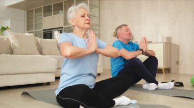 Yoga farkındalığı meditasyonu. Yetişkin bir çift evde yoga yapıyor. Orta yaşlı koca karısı nilüferde oturmuş yoga minderinde meditasyon yaparken poz veriyor. Aile nefes egzersizi yapıyor.
