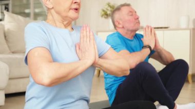 Yoga farkındalığı meditasyonu. Yetişkin bir çift evde yoga yapıyor. Orta yaşlı koca karısı nilüferde oturmuş yoga minderinde meditasyon yaparken poz veriyor. Aile nefes egzersizi yapıyor.