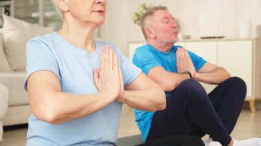 Yoga farkındalığı meditasyonu. Yetişkin bir çift evde yoga yapıyor. Orta yaşlı koca karısı nilüferde oturmuş yoga minderinde meditasyon yaparken poz veriyor. Aile nefes egzersizi yapıyor.
