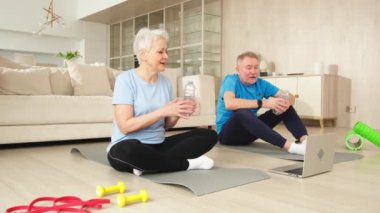 Yoga farkındalık suyu. Yetişkin bir çift, internetten yoga yaptıktan sonra su içiyor. Yaşlı eş idmandan önce su içer. Aile evde spor yapıyor.