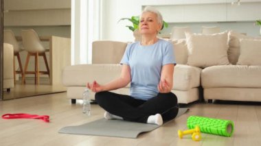 Yoga farkındalığı meditasyonu. Yetişkin bir kadın evde yoga yapıyor. Orta yaşlı kadın nilüfer çiçeğinde oturmuş yoga minderinde meditasyon yaparken poz veriyor. Yaşlı orta yaşlı kadın nefes egzersizi yapıyor.