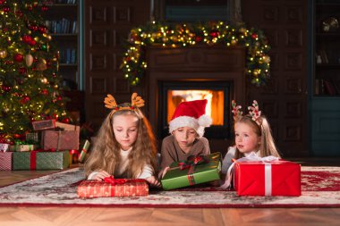 Mutlu Noeller Noel tatili. Çocuklar Noel ağacının yanındaki hediye kutusunu açıyor. Oturma odasında Noel ağacı şöminesi olan çocuklar sürpriz yüzlü hediye kutusunu açıyorlar. Evde Noel arifesi