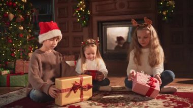 Mutlu Noeller Noel tatili. Çocuklar Noel ağacının yanındaki hediye kutusunu açıyor. Oturma odasında Noel ağacı şöminesi olan çocuklar sürpriz yüzlü hediye kutusunu açıyorlar. Evde Noel arifesi
