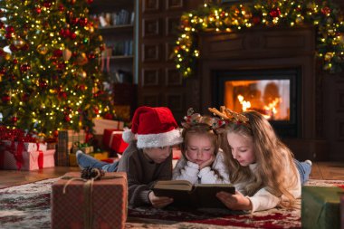 Mutlu Noeller Noel tatili. Erkek kardeşler çocuklar çocuklar Noel ağacının yanında kış akşamı şömineli oturma odasında sihirli noel kitabı okuyorlar. Evde Noel arifesi