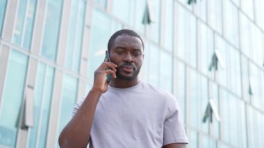Üzgün, yalnız, hayal kırıklığına uğramış Afrikalı bir adam şehir caddesinde tek başına akıllı telefondan konuşuyor. Üzüntüden kötü haberler alan mutsuz bir insan cep telefonuyla telefona cevap veriyor. Stresli adam.