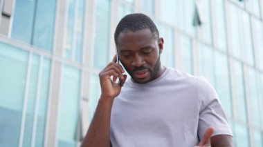 Üzgün, yalnız, hayal kırıklığına uğramış Afrikalı bir adam şehir caddesinde tek başına akıllı telefondan konuşuyor. Üzüntüden kötü haberler alan mutsuz bir insan cep telefonuyla telefona cevap veriyor. Stresli adam.